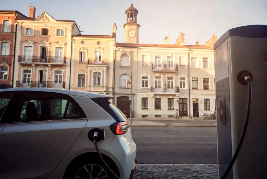 Concepto de auto eléctrico compacto y económico cargando en una ciudad europea, representando modelos como el VW ID.2all o Renault Twingo. Vehículos eléctricos 2026: Análisis