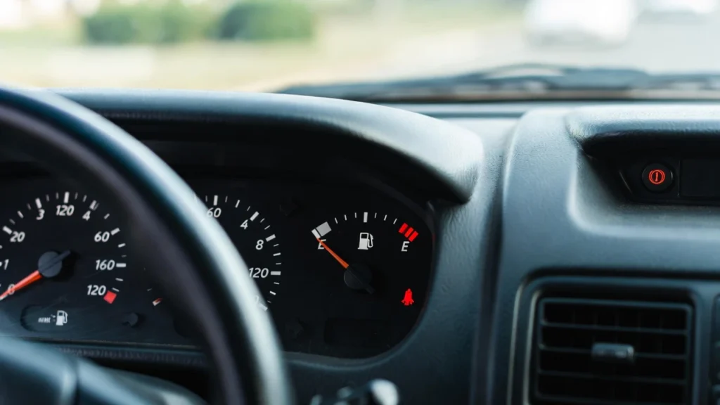 1a3ae1ae-2035-4e05-9989-343e27b3141f Primer plano del panel de instrumentos de un coche, mostrando el indicador de combustible casi vacío y la luz roja de reserva encendida.